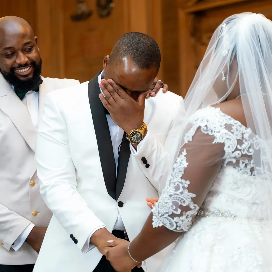 Groom reacting emotionally during the ceremony after winning a wedding raffle, holding his bride’s hand with the best man smiling supportively.