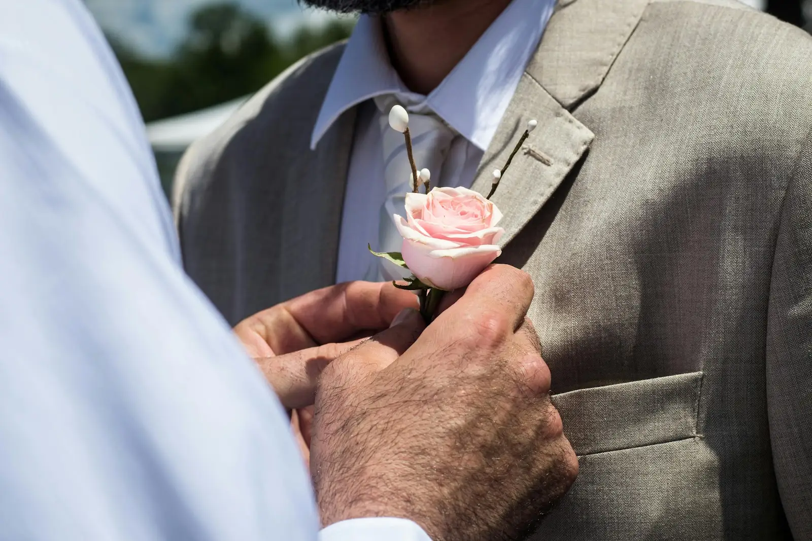 Elegant groom in gray suit holding pink rose boutonniere at wedding raffles ceremony