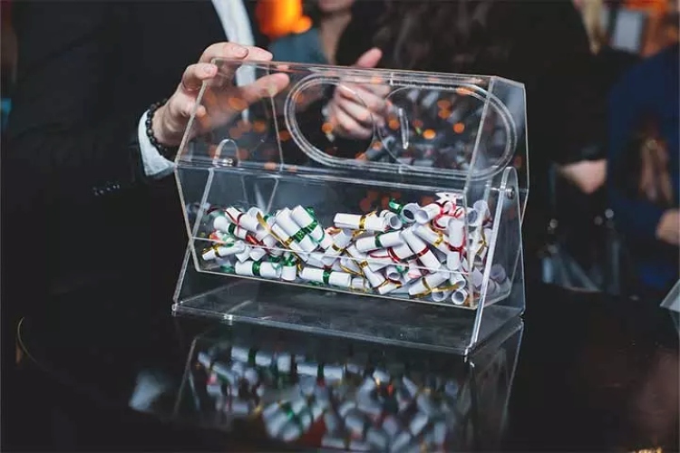 Guests participating in a live draw for UK wedding raffle competitions, selecting scrolls from a transparent raffle box