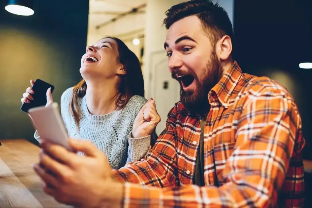 A cheerful couple celebrating while looking at a smartphone—capturing the joy that can come when you enter a wedding raffle competition and actually win.