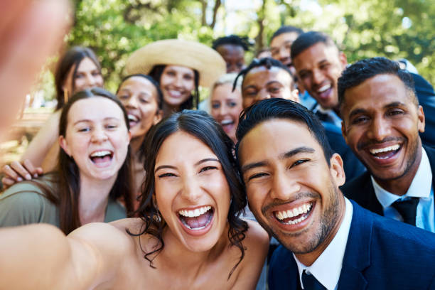 Diverse group of wedding guests taking joyful selfie together outdoors, capturing the fun moments and connections that define a truly unforgettable wedding guest experience filled with laughter and celebration.