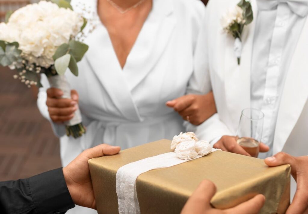 A couple presenting a wrapped gift to a guest as a wedding guest gift.