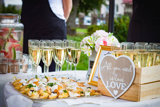 A wedding table with champagne and appetizers, featuring a "All you need is love" sign, carefully chosen to personalise your wedding's culinary experience.