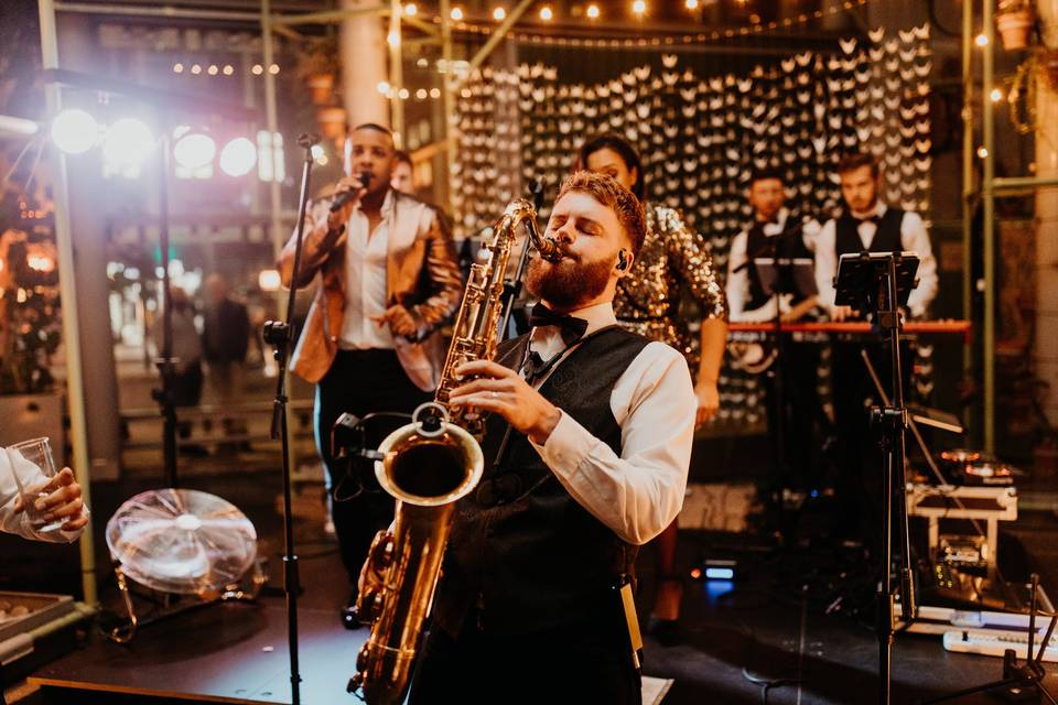 A band with a saxophonist performing at a wedding reception, providing entertainment that helps personalise your wedding.