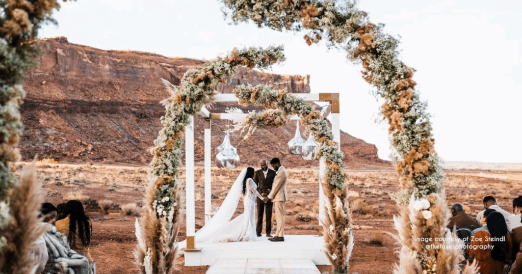 A wedding arch adorned with flowers frames a couple during their outdoor ceremony, reflecting one of the beautiful wedding trends.