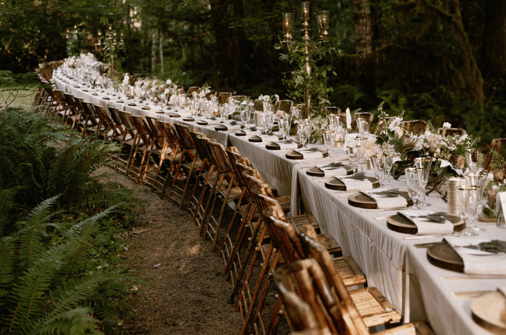 An elegantly set long table for a wedding reception in a lush outdoor setting, exemplifying modern eco-friendly wedding trends.