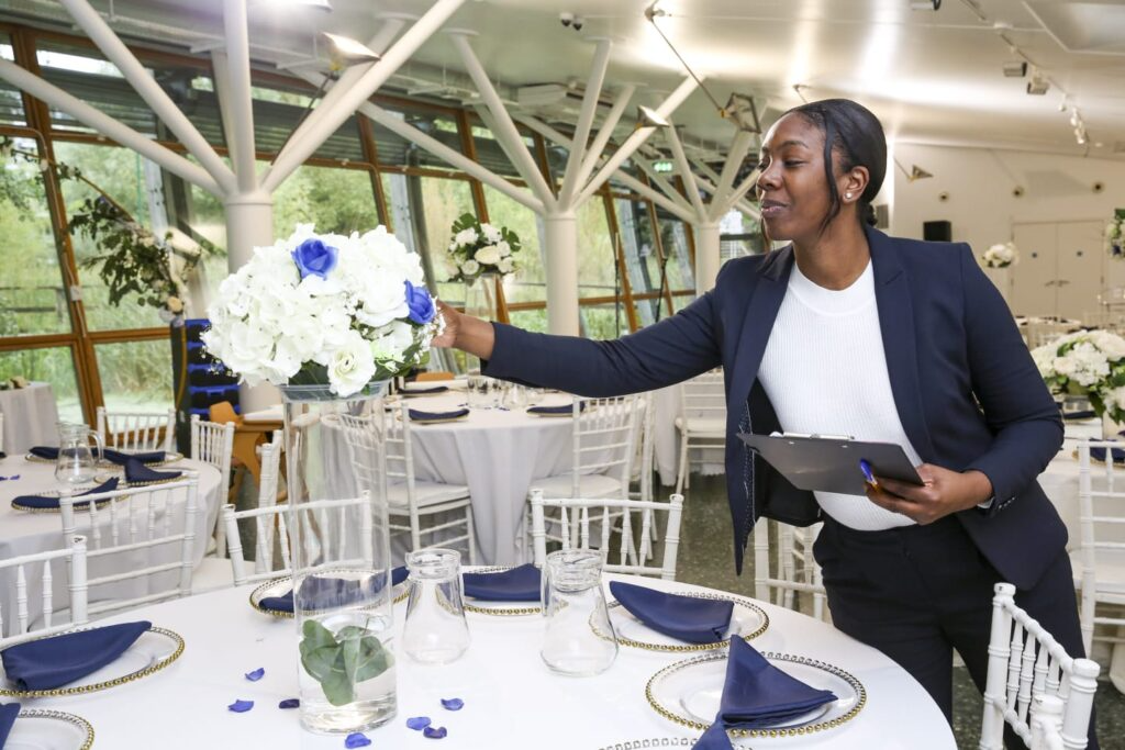 A professional wedding planner meticulously arranging a white and blue floral centerpiece on a beautifully set table, ensuring every detail is perfect before guests arrive.