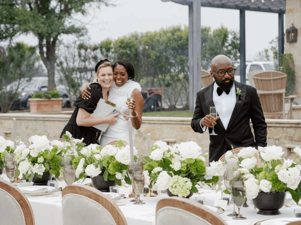 A joyous scene at a wedding reception where a wedding planner is seen embracing a bride and groom, with beautifully decorated tables in the foreground, summarizing the emotional rewards of their work.
